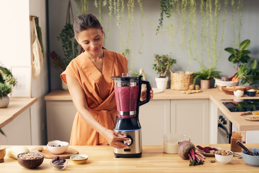 young-female-pressing-start-button-of-blender-while-cooking