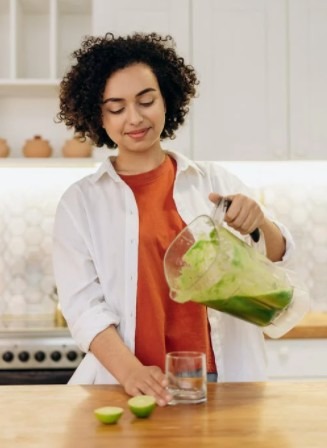 a woman in white button up long sleeve shirt pouring fresh drink in a glass