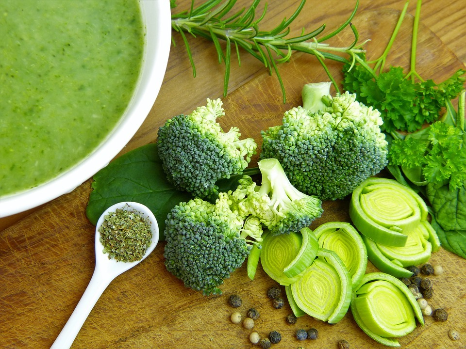 a bowl of broccoli soup along with some raw broccoli and leek