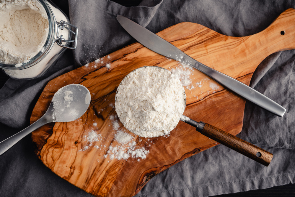Directly above one cup full of flour with spoon, knife, cutting board, and jar of flour
