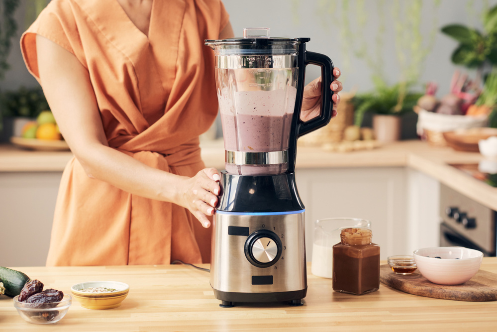 Hand of young woman preparing smoothie in blender