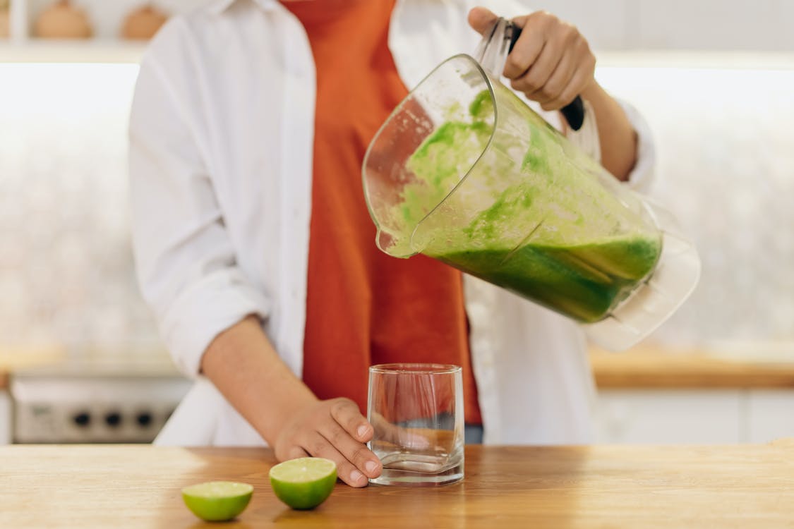 a person pouring a green smoothie from a blender into a glass