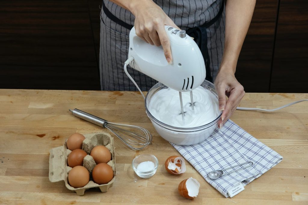 a woman using a hand blender to whisk egg whites 