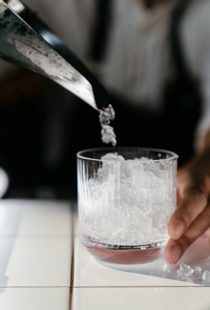 person pouring crushed ice on clear drinking glass